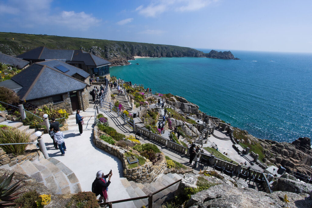 People walking around an open air theatre with sea in background.